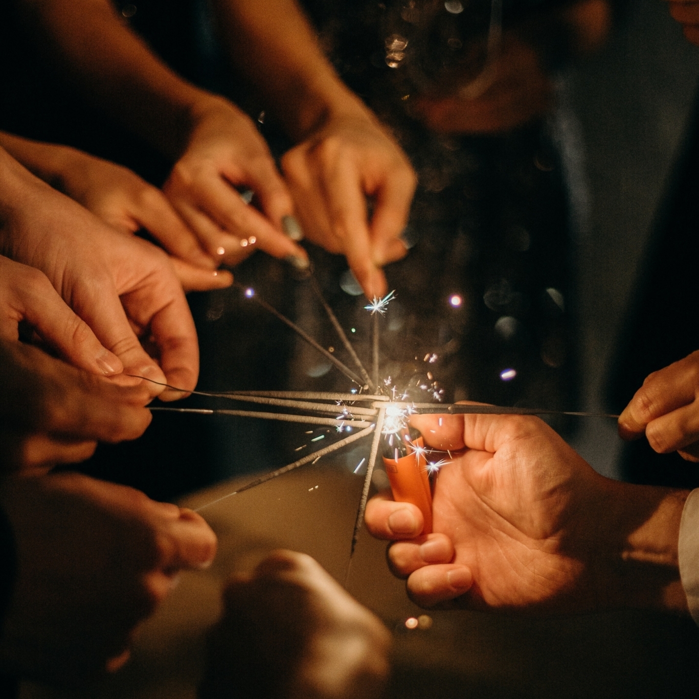 Eine Gruppe von Menschen, die Wunderkerzen eng beieinander halten, erzeugt vor einem dunklen Hintergrund ein helles und festliches Lichtspiel. Mehrere Hände sind sichtbar, was auf eine fröhliche Familienfeier oder ein feierliches Ereignis schließen lässt. Hotel Schloss Burgellern
